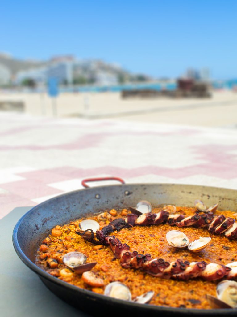 Arroz con pulpo y almejas en paellera, con la playa de Cullera al fondo