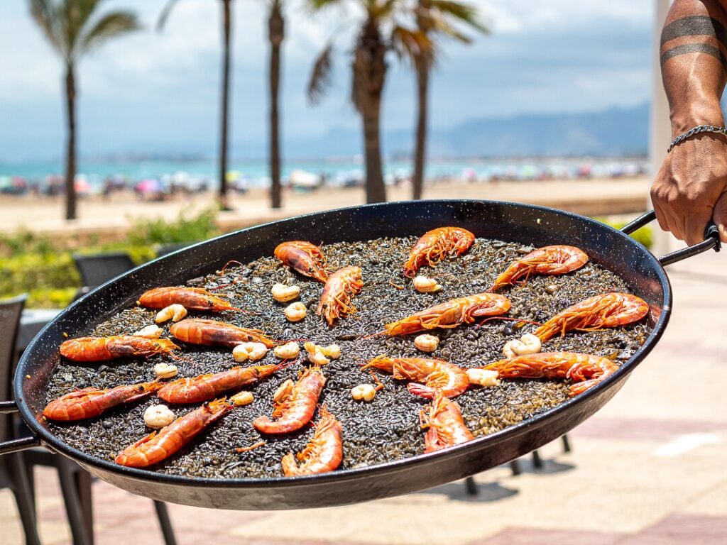Arroz negro con gambas a la plancha servido en paellera frente al mar